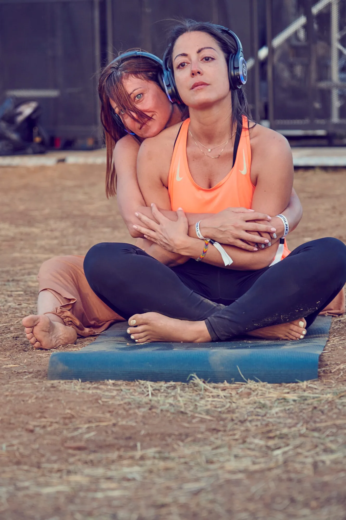 Due partecipanti abbracciate su un tappetino a un festival, con cuffie wireless