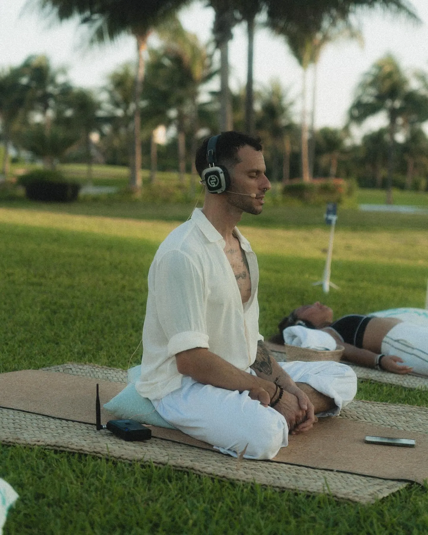 Teacher sitting on a mat with a headset microphone and a portable transmitter beside him